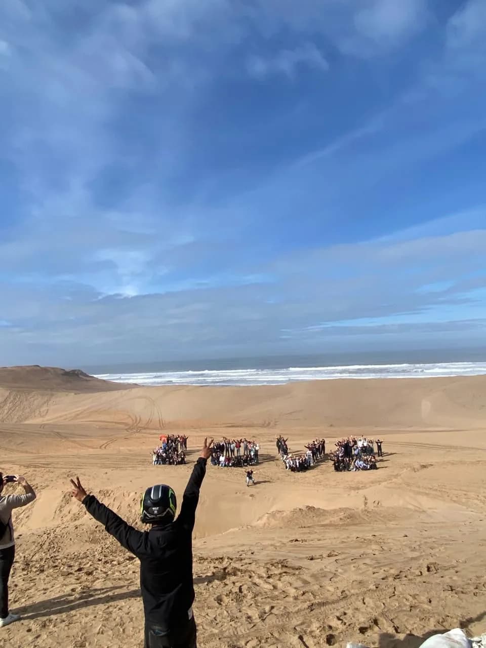 El grupo reunido en una duna sobre la playa, con los brazos en alto y el océano detrás.