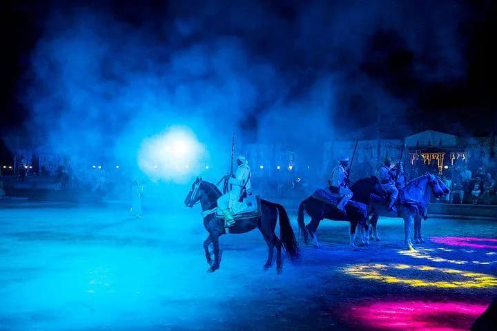 Des cavaliers traversant l'arène dans une lumière bleue et de la fumée.